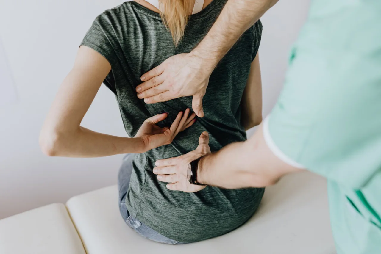A practitioner examines a patient's lower spine with both hands.