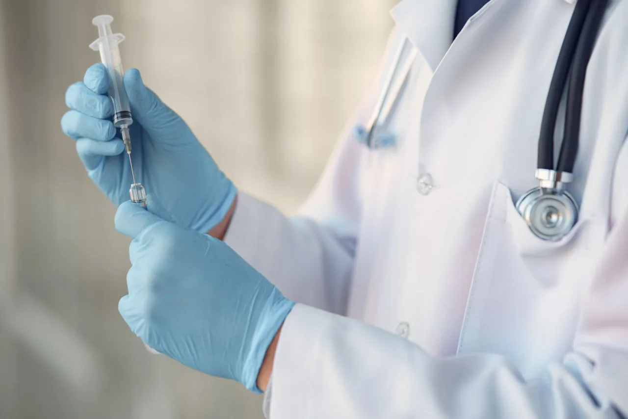 Gloved hands of a clinician holding a syringe