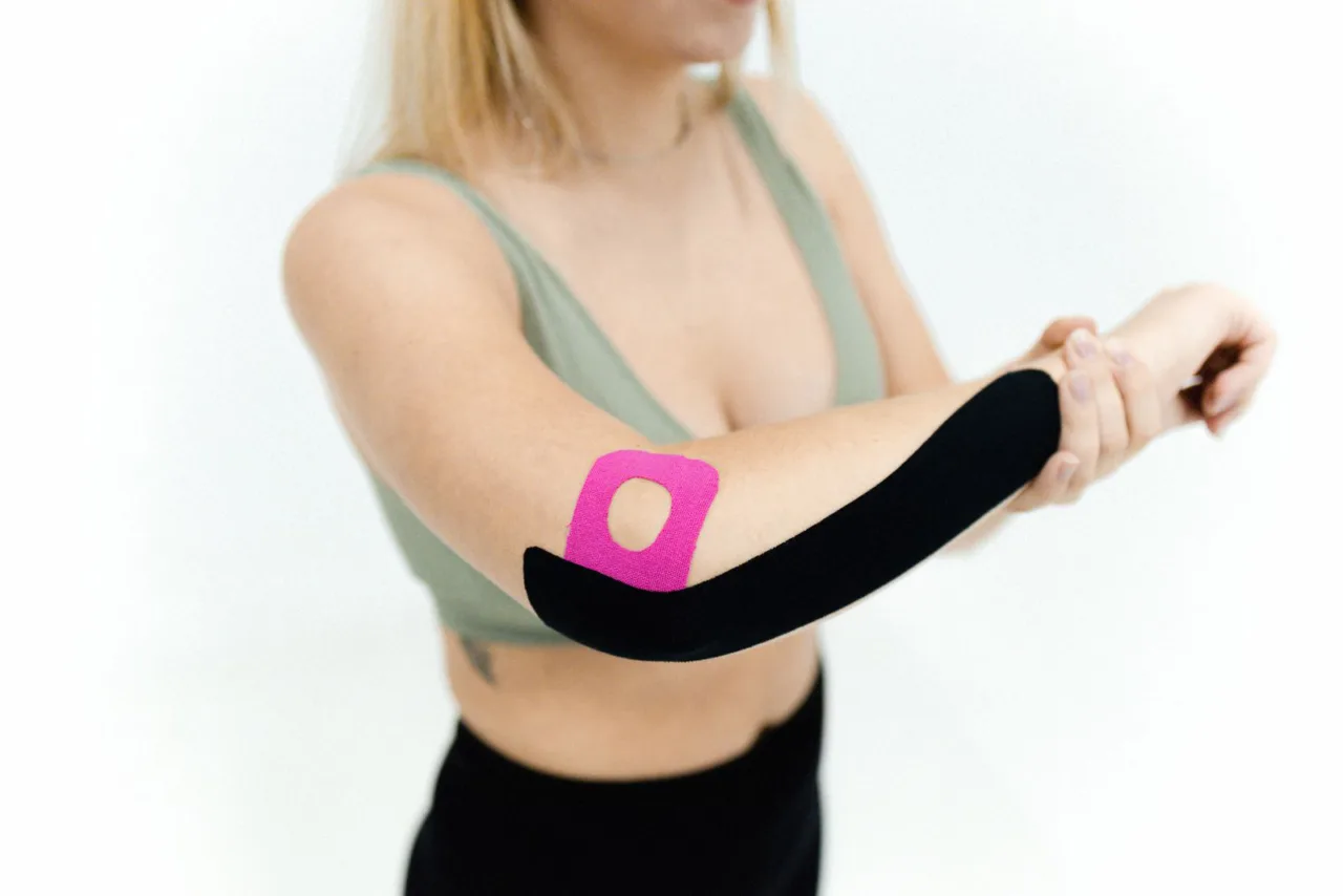A woman applies kinesiology tape along her own forearm.