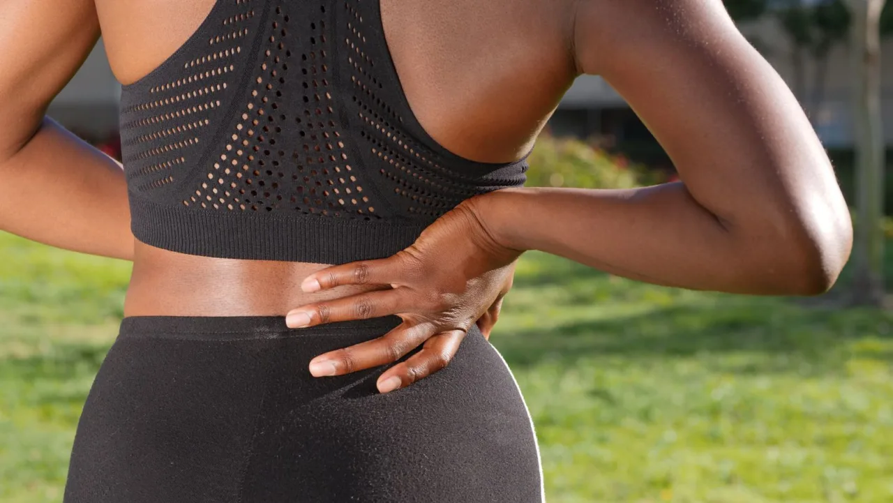 A woman in exercise clothing presses both hands to her lower back.