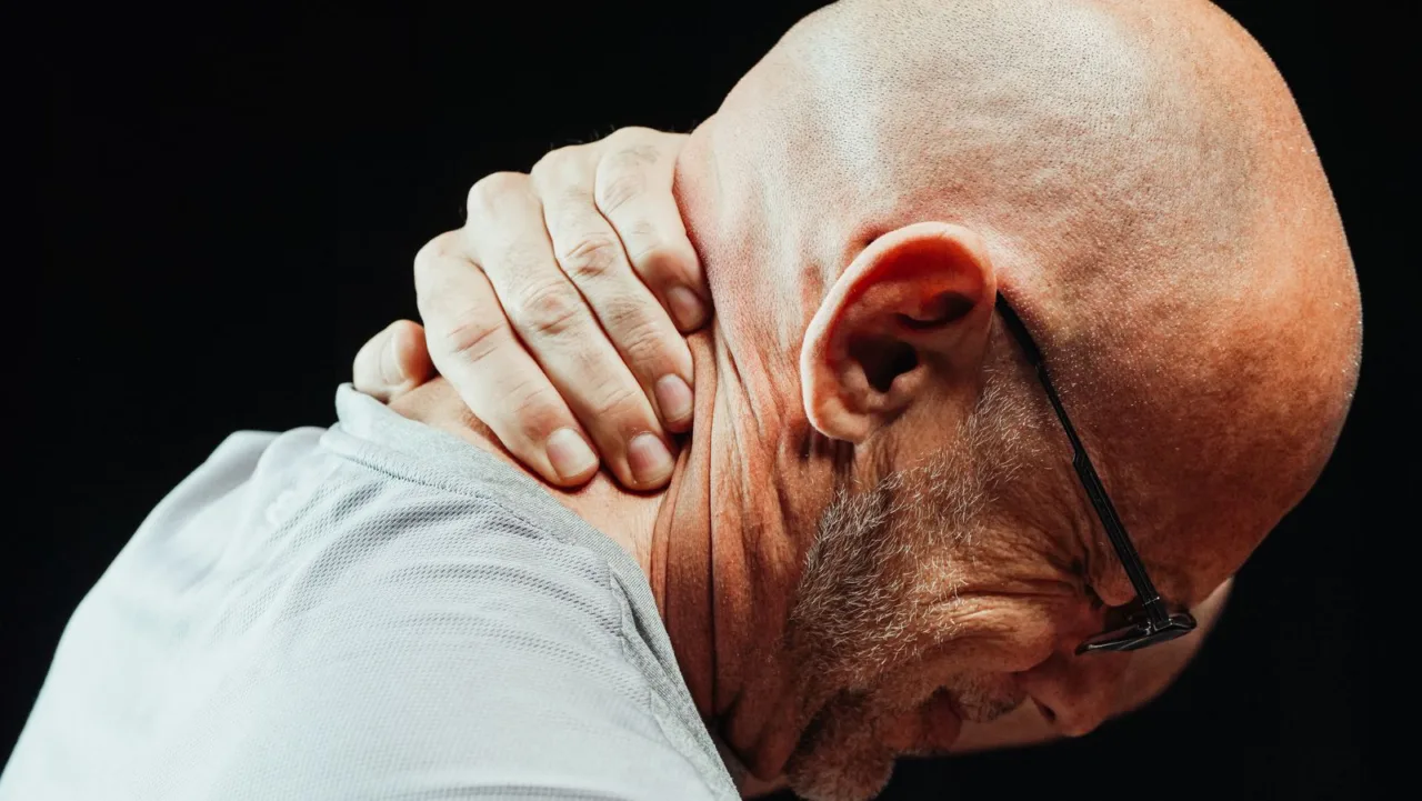 A man holds the back of his neck with both hands.