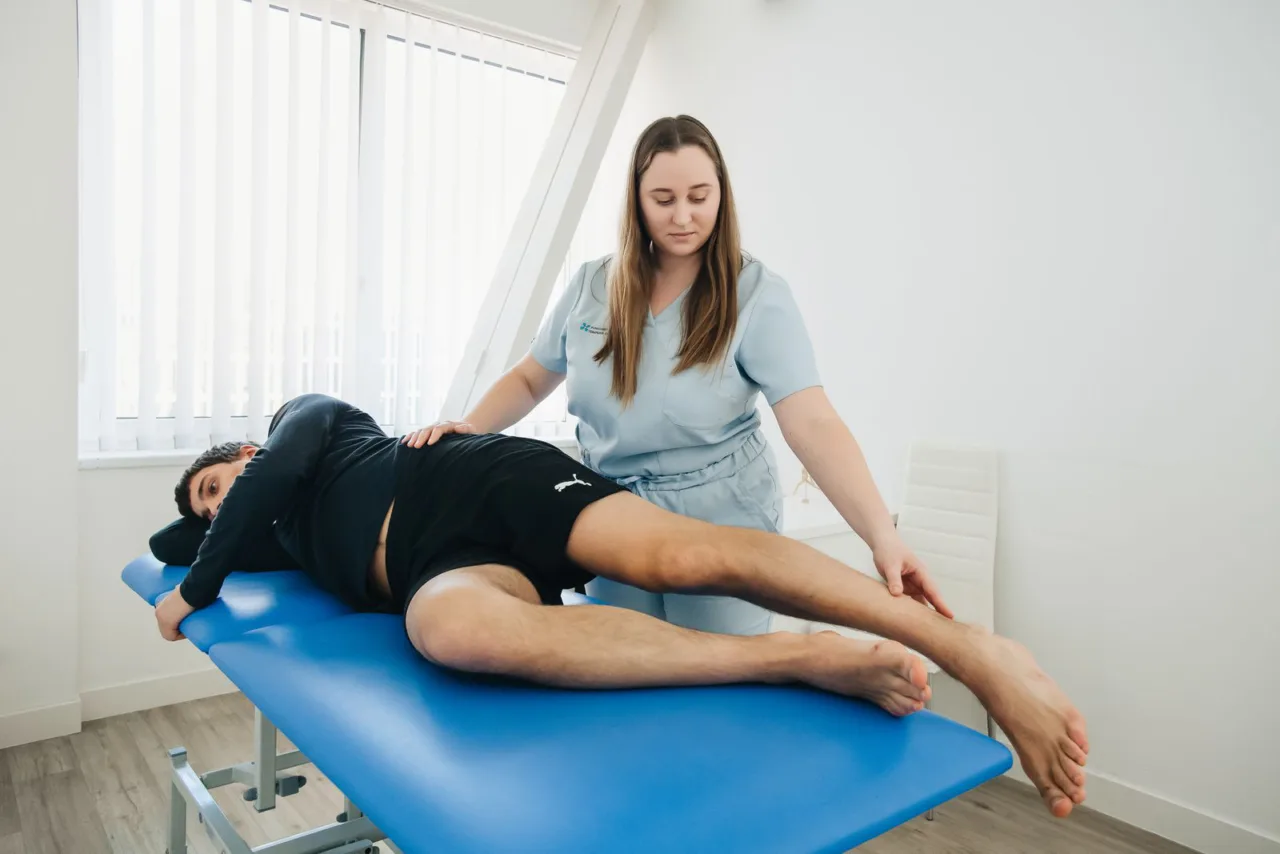 A physical therapist supervises a patient exercising on a mat.