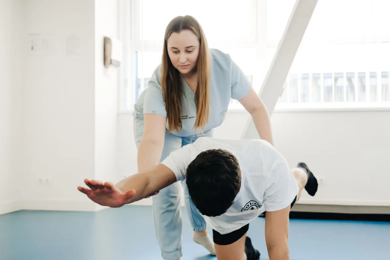 A physical therapist guides a patient through a supported stretch in a treatment room.