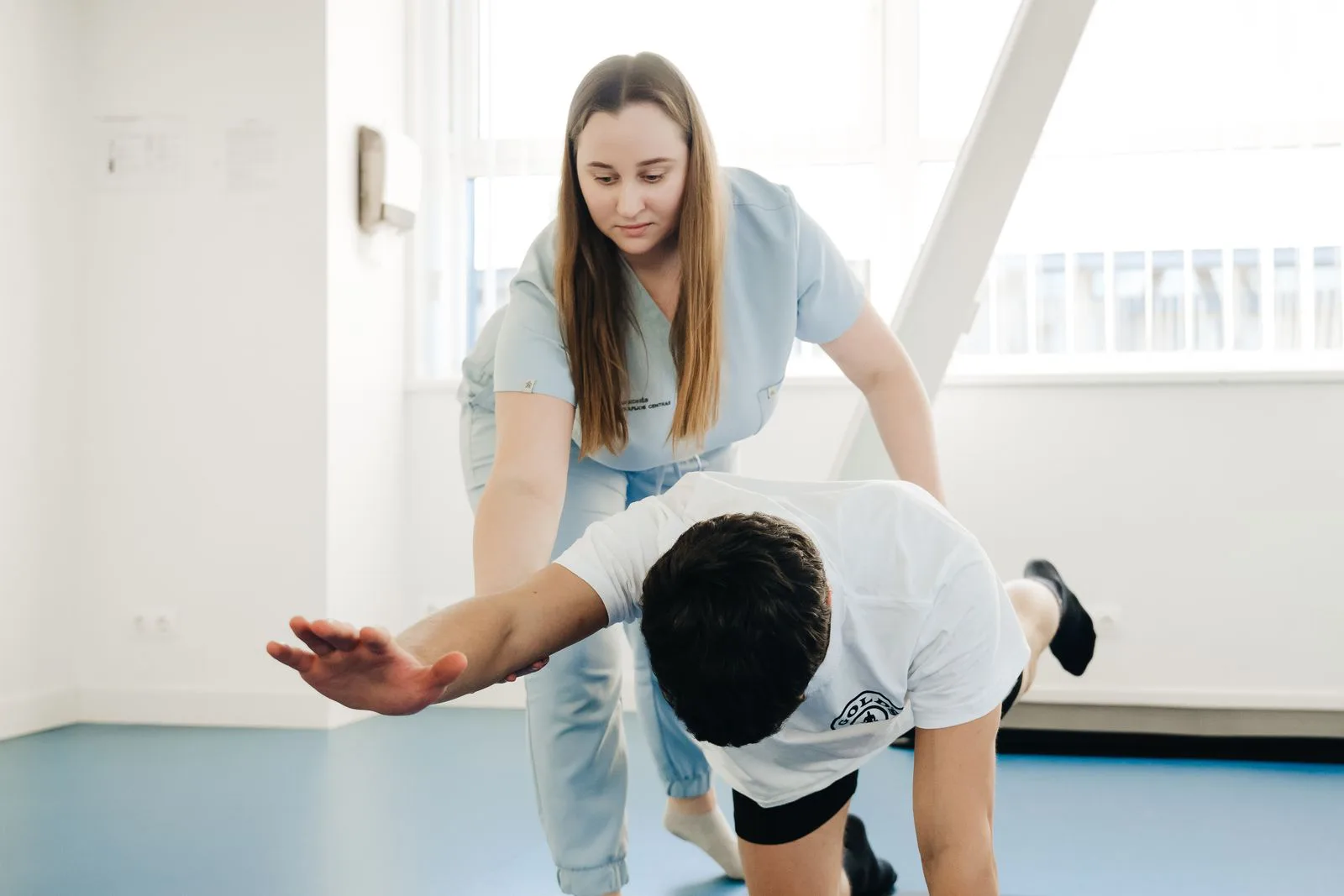 A physical therapist guides a patient through a supported stretch in a treatment room.