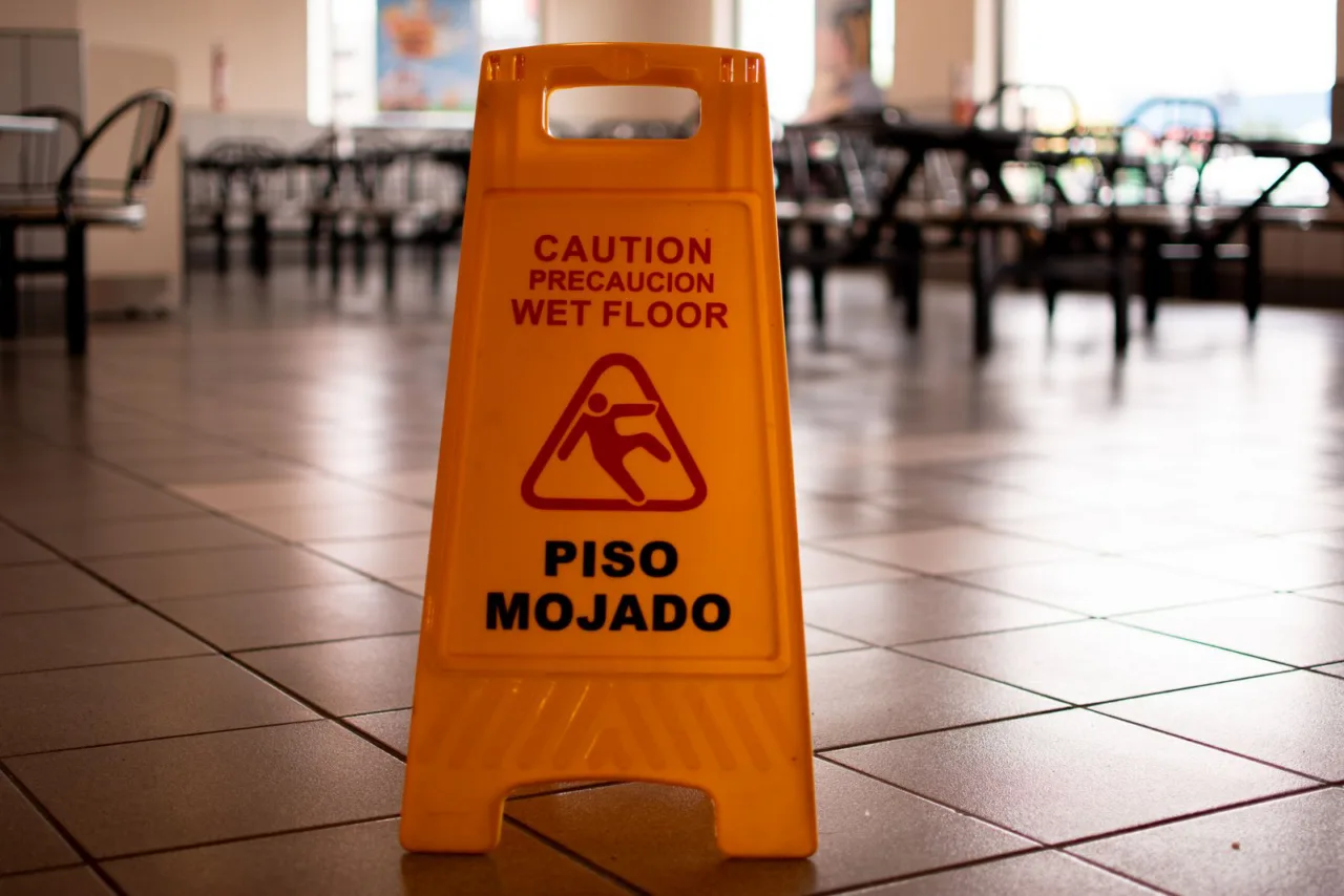 A yellow caution sign warns of a wet floor in English and Spanish.