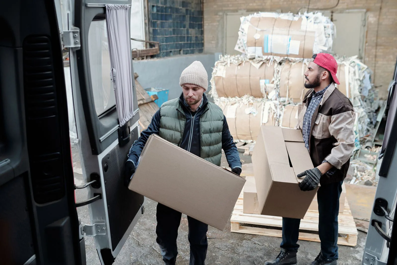 Two workers lift cardboard boxes out of a delivery van.
