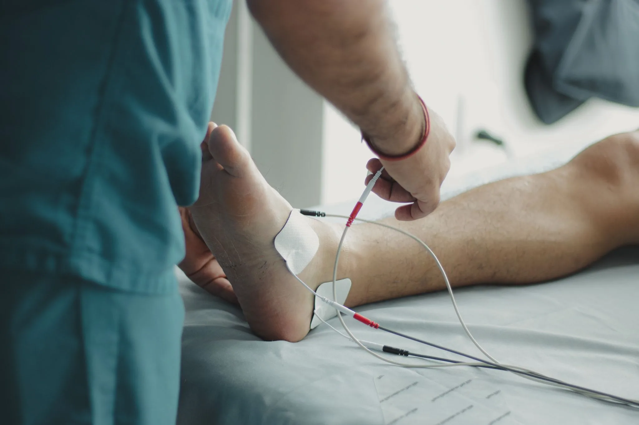 A clinician connects electrodes on a patient's foot for a nerve conduction test.