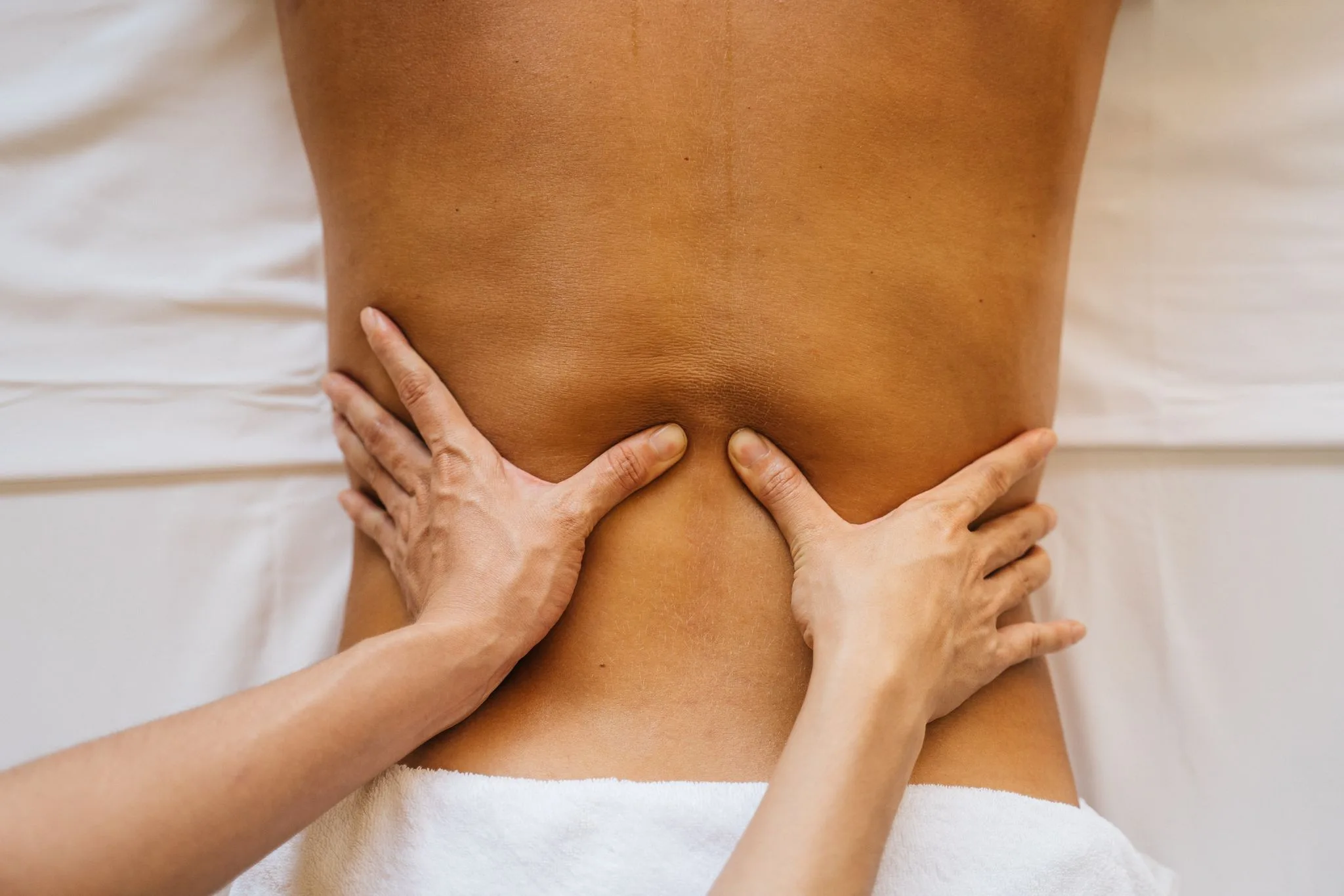 A therapist's hands press on both sides of a patient's lower back.